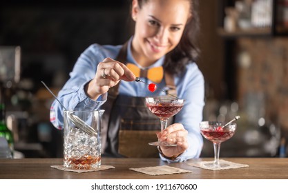 Smiling barmaid wearing wooden bow tie decorates manhattan cocktail drink with a cherry. - Powered by Shutterstock