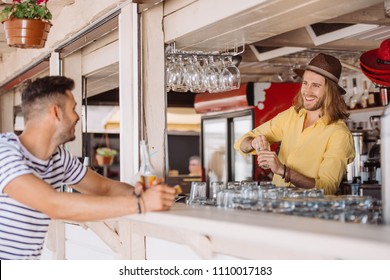 smiling bartender and client with beer bottle looking at each other in beach bar - Powered by Shutterstock