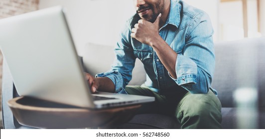 Smiling bearded African man working at home while sitting on the sofa.Concept of young people using mobile devices.Blurred background.Cropped - Shutterstock ID 562748560