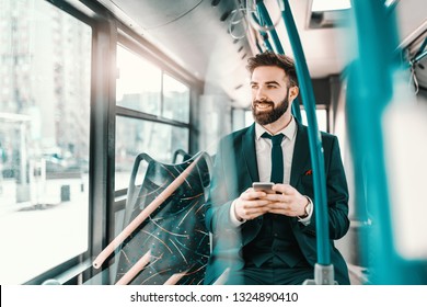 Smiling Bearded Caucasian Businessman In Formal Wear Sitting In Public Transport And Using Smart Phone.