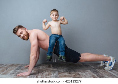 Smiling bearded father doing push-ups with little son sitting on his back over grey background - Powered by Shutterstock