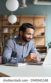 Smiling Bearded Indian Businessman Working On Laptop At Home Office. Young Indian Student Using Computer Remote Studying, Virtual Training On Video Call Meeting, Watching Online Webinar Or Seminar.