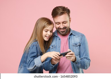 Smiling bearded man in casual clothes with cute child baby girl. Father little kid daughter isolated on pastel pink background. Love family parenthood childhood concept. Play game with mobile phone - Powered by Shutterstock