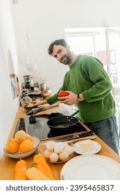 Smiling and bearded man in casual clothes looking at camera while holding bell pepper near eggs - Shutterstock ID 2395465837
