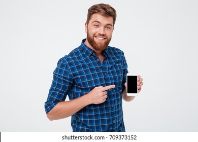 Smiling Bearded man in checkered shirt showing blank smartphone screen and pointing at him while looking at the camera over gray background - Powered by Shutterstock