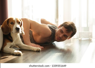 Smiling bearded man doing exercises against the window at home with his dog - Powered by Shutterstock