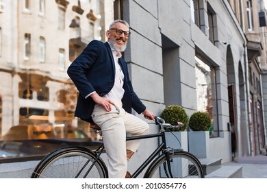 smiling bearded man in glasses posing with hand on hip and riding bicycle on urban street - Powered by Shutterstock