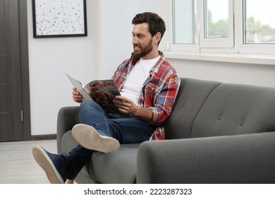 Smiling Bearded Man Reading Magazine On Sofa At Home