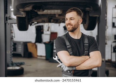 Smiling bearded mechanic while standing with crossed arms and holding wrenches in a car service - Powered by Shutterstock