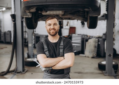 Smiling bearded mechanic while standing with crossed arms and holding wrenches in a car service - Powered by Shutterstock
