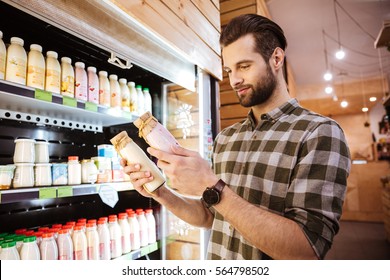 Smiling bearded young man choosing yogurt in grocery shop
