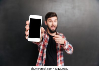 Smiling Bearded Young Man Holding And Showing Blank Screen Cell Phone Over Grey Background