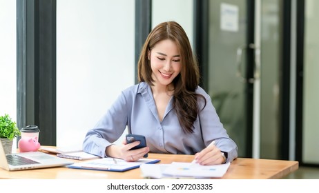 Smiling beautiful Asian businesswoman analyzing chart and graph showing changes on the market and holding smartphone at office. - Powered by Shutterstock