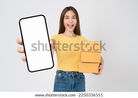 Smiling beautiful Asian woman holding cardboard boxes and hands show smartphone mockup of blank screen on white background. Take your screen to put on advertising. Concept delivery online.
