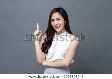 Smiling beautiful Asian woman pointing finger upward to empty space in studio gray isolated background