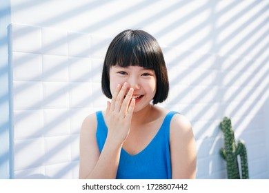 Smiling Beautiful Bob Haircut Asian Woman In Blue Tank Top Shirt Cover Her Mouth And Laughing Over White Tiles Wall Background.