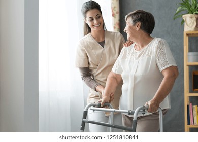 Smiling beautiful caregiver and disabled old lady with walker at home