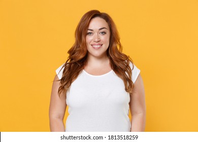 Smiling beautiful charming young redhead plus size body positive woman 20s in white blank design casual t-shirt posing looking camera isolated on yellow color background studio portrait