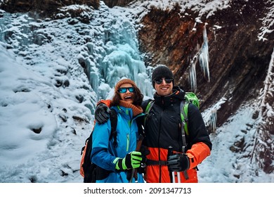 Smiling Beautiful Couple Dressed In Warm Winter Sportswear, Sunglasses And Gloves Holding Trekking Poles, Looking At The Camera And Smiling. Tourism, Recreation, Sports.