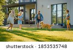 Smiling Beautiful Family of Four Play Fetch flying disc with Happy Golden Retriever Dog on the Backyard Lawn. Idyllic Family Has Fun with Loyal Pedigree Dog Outdoors in Summer House Backyard