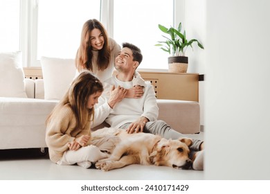 Smiling beautiful family, young mother, father and little daughter relaxing together, woman hugging man, little girl petting and playing with dog, golden retriever. Concept of love, parenthood - Powered by Shutterstock