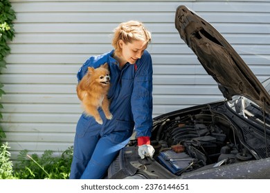 smiling beautiful female mechanic holding small dog sitting on car hood - Powered by Shutterstock