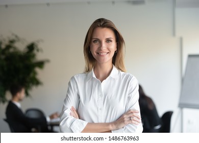 Smiling beautiful female professional manager standing with arms crossed looking at camera, happy confident business woman corporate leader boss ceo posing in office, headshot close up portrait