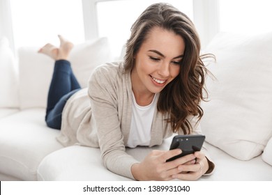 Smiling Beautiful Girl Relaxing On A Couch At Home, Using Mobile Phone