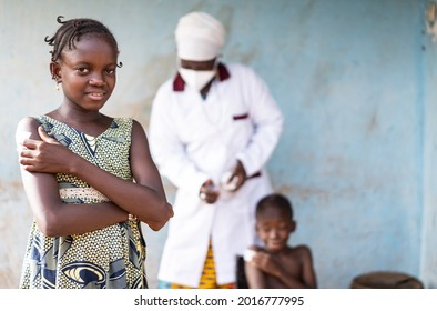 A Smiling Beautiful Little African Girl Is Holding A Patch On Her Shoulder After Getting A Flu Shot, With A Standing Black Nurse In Hospital Uniform Wearing A Face Mask