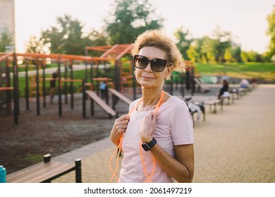 Smiling Beautiful Mature Woman With Skipping Rope Posing Against Backdrop Of Street Gym After Workout. Older Woman With A Jumping Rope Ready For Training. Portrait Of A Sporty Smiling Mature Woman.