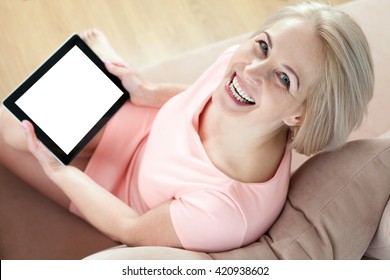 Smiling Beautiful Middle Aged Woman Sitting On Couch With Tablet White S?reen And Looking Up. Unusually Top View