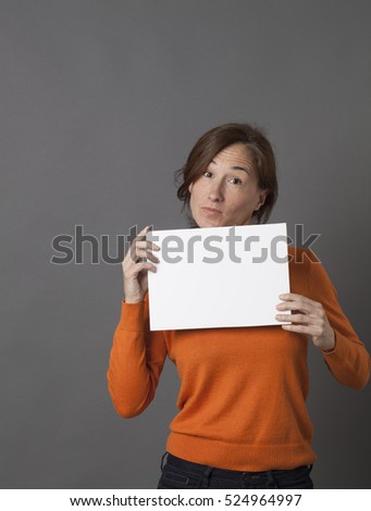 smiling beautiful middle aged woman holding a blank message panel with surprising copy space text, grey background