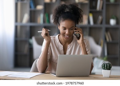 Smiling beautiful millennial african mixed race businesswoman working on computer, giving professional consultation to client or discussing project issues remotely with partners by telephone call.