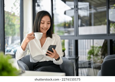 Smiling and beautiful millennial Asian businesswoman using her phone and having coffee in the coffee shop. lifestyle concept - Powered by Shutterstock