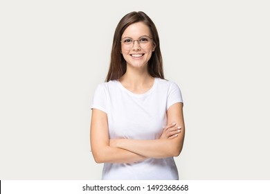 Smiling Beautiful Millennial Girl Wear Glasses And White T-shirt Stand With Arms Crossed Isolated On Grey Studio Background, Happy Young Woman In Spectacles Look At Camera Posing Or Casting