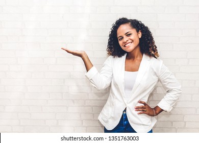 Smiling Beautiful Professional Business African American Black Woman Showing Empty Copy Space On Open Hand Standing Near White Brick Wall Background