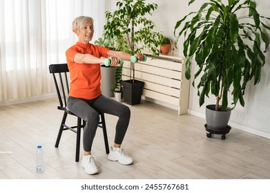 Smiling beautiful senior woman health instructor doing chair exercises with dumbbells - Powered by Shutterstock