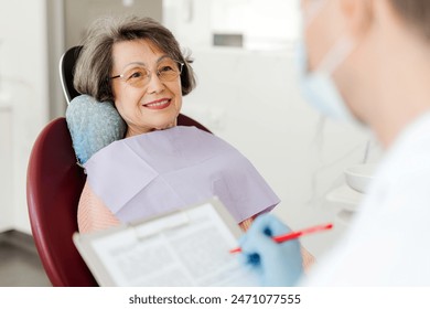 Smiling, beautiful senior woman sitting in dental chair on visit to dentist, talking in modern dentistry. Concept of dental care - Powered by Shutterstock