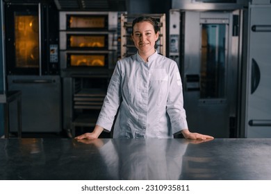 smiling beautiful woman baker in uniform stands near the oven before the start work bakery production of pastries - Powered by Shutterstock