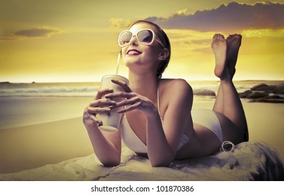 Smiling beautiful woman in bikini lying on a beach and holding a refreshing drink