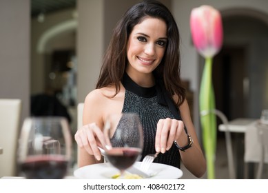 Smiling beautiful woman having dinner in a restaurant. Flower in the foreground