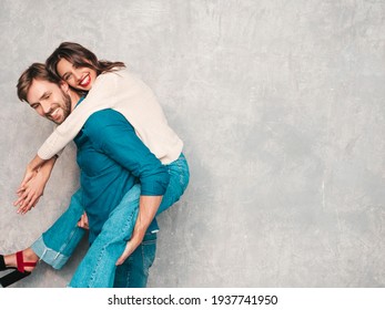 Smiling beautiful woman and her handsome boyfriend.Happy cheerful family having tender moments near grey wall in studio.Pure models hugging.Embracing each other.Male gives piggyback riding
