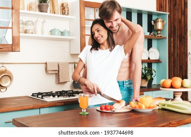 Smiling beautiful woman and her handsome boyfriend.Happy cheerful loving family having tender moments.Pure models making breakfast.Embracing each other.Cooking together in light kitchen at home