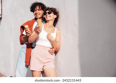 Smiling beautiful woman and her handsome boyfriend. Woman in casual summer clothes. Happy cheerful family. Couple posing on the street background at sunny day. Eating tasty ice cream in waffles cone - Powered by Shutterstock