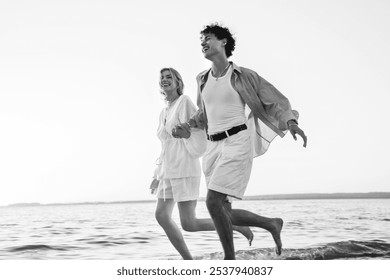 Smiling beautiful woman and her handsome boyfriend. Excited couple in casual clothes. Happy cheerful family. Female and man run at sunrise over sea beach outdoors. Seaside in summer day, monochrome  - Powered by Shutterstock