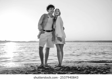 Smiling beautiful woman and her handsome boyfriend. Excited couple in casual clothes. Happy cheerful family. Female and man pose at sunrise over sea beach outdoors. Seaside in summer day, monochrome  - Powered by Shutterstock