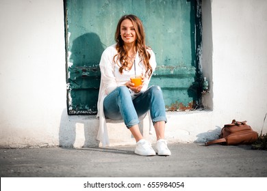 Smiling beautiful woman holding cup orange juice, sitting outdoor, healthy lifestyle, warmly, daytime - Powered by Shutterstock