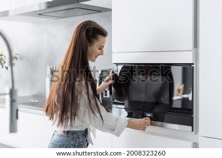 Smiling beautiful woman housewife preparing food in electric microwave oven, adjusting temperature on it. Happy female using modern kitchen built-in appliance Foto d'archivio © 