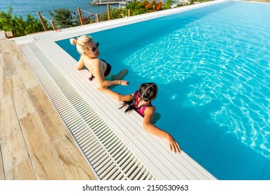 Smiling beautiful woman smears with cream for sunburn little girl near pool in aquapark