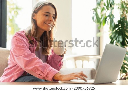 Smiling beautiful woman, successful copywriter using laptop computer, typing on keyboard working freelance project online. Student studying, learning language holding cup of coffee. Online education